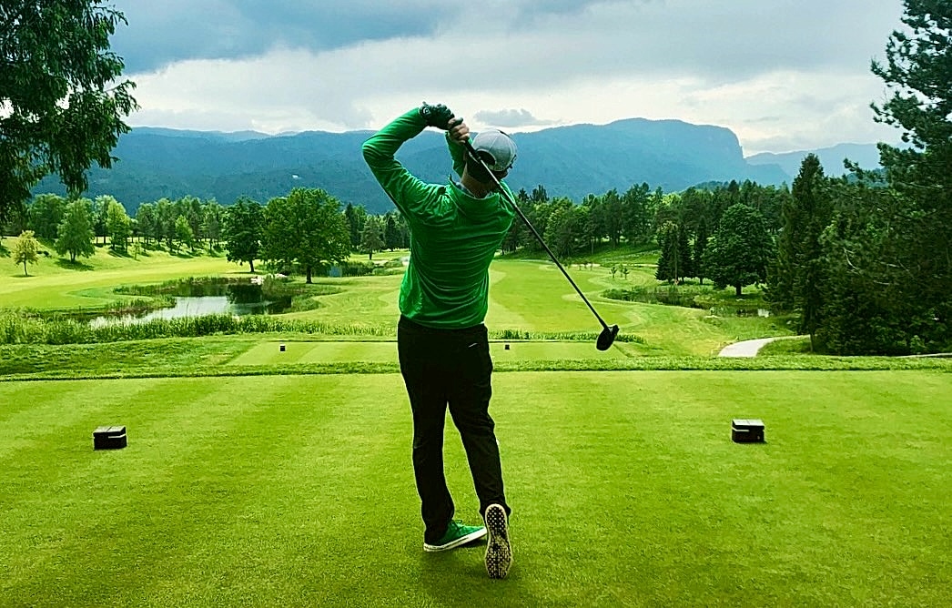 Golfer mid-swing on a mountain course at sunrise